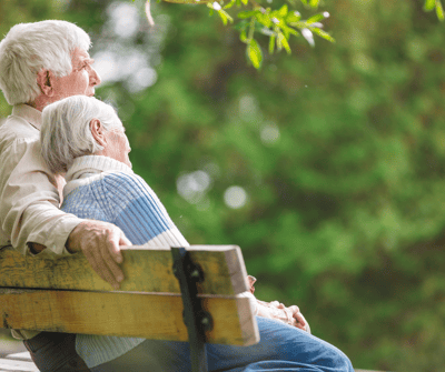 An elderly couple sitting together on a bench outdoors