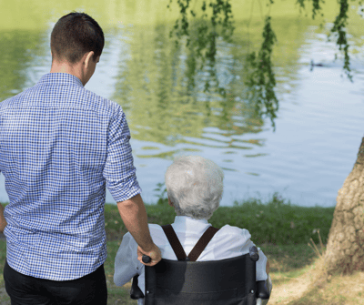 A caregiver pushing a resident in a wheelchair by the lake