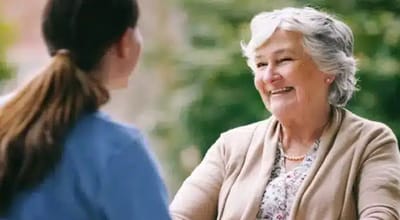 Senior woman smiling with caregiver outdoors.