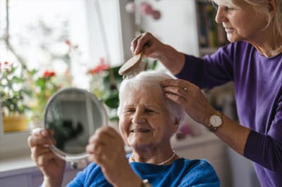 A caregiver brushing the hair of a smiling senior resident