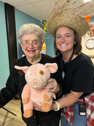 Resident holding a stuffed pig with staff member, smiling