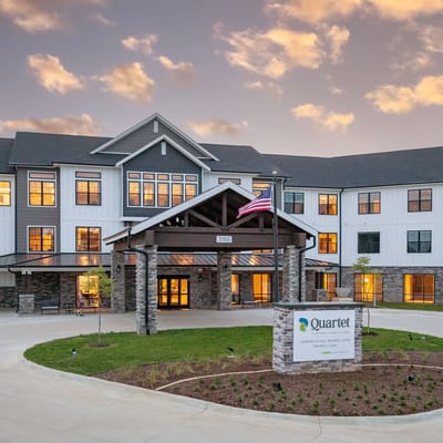 Quartet – A Senior Living Village, assisted living in Bettendorf, IA — Senior living facility entrance with decorative landscaping and flag