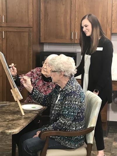 Residents painting with staff assistance in an activity room