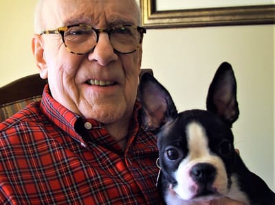 A senior man smiling with a dog in a cozy setting