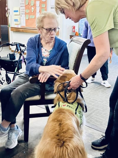 A resident interacting with a therapy dog and staff member