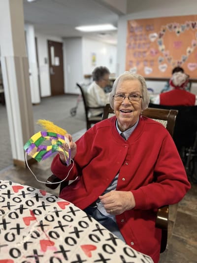 Resident smiling with a colorful craft in an activity room