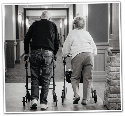 Two residents walking with walkers in a hallway