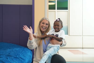 A staff member and child smiling in a facility common area