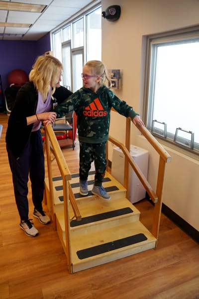 A staff member assisting a child on a balance beam in therapy