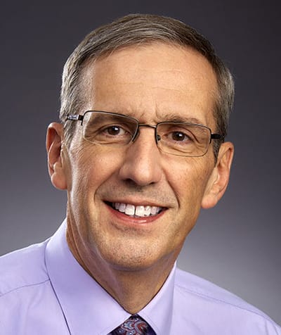 Professional headshot of a smiling man in glasses
