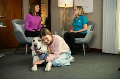 Residents and staff interacting with a therapy dog in a cozy common area