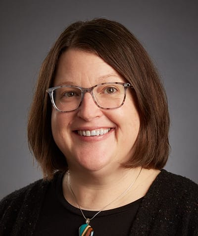 A woman smiling with glasses and a black top