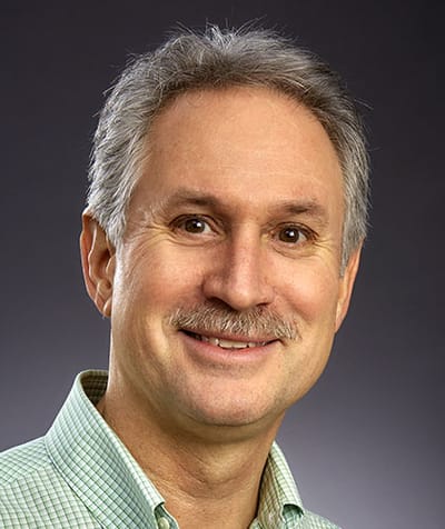 A smiling man with a mustache in a green shirt