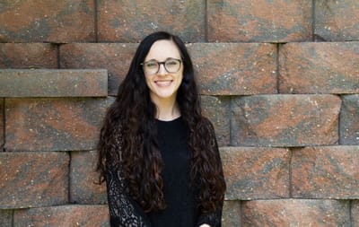 A smiling woman posing in front of a stone wall