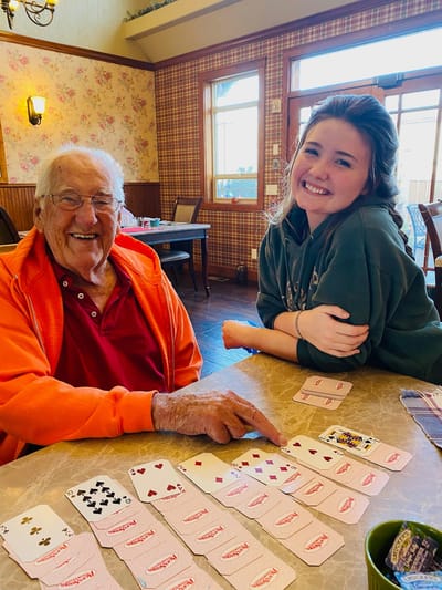 Senior resident playing cards with staff in a common area