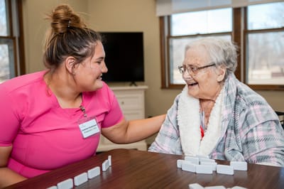 Resident playing dominoes with staff in a common area