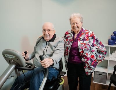 A senior resident using fitness equipment with staff assistance