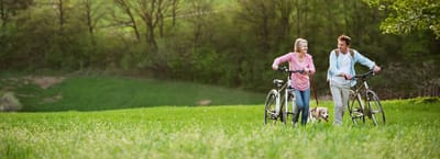Two seniors walking with bicycles in a grassy field