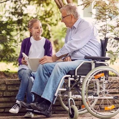 A senior man in a wheelchair talks to a young girl outside