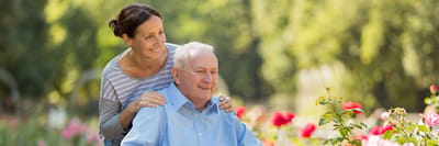 Elderly man in wheelchair with caregiver in a garden.