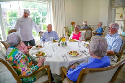 Residents enjoying dinner with a chef in a dining room