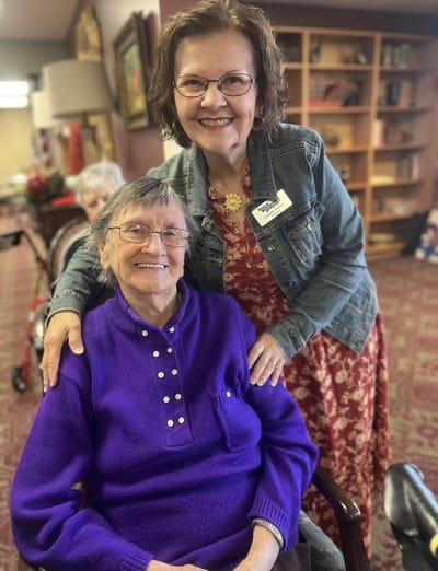 A staff member posing with a resident in a cozy indoor setting