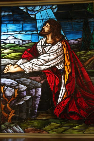 Stained glass depiction of a religious figure in prayer