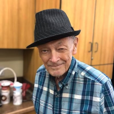 A senior man smiling while wearing a hat in a kitchen