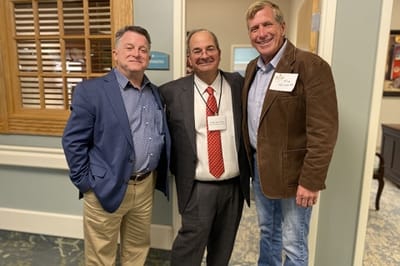 Three men in professional attire posing in a hallway