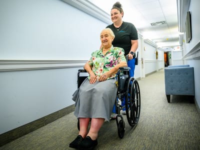 Staff assisting a resident in a wheelchair in a hallway