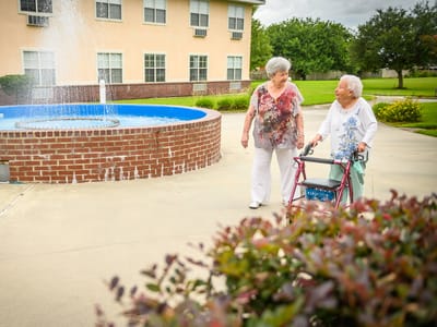 Two senior residents walking near a fountain in the garden