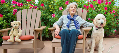 Senior resident enjoying time outside with a dog and a teddy bear