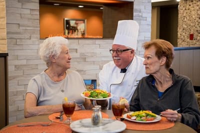 Residents enjoying a meal with a chef in a dining area