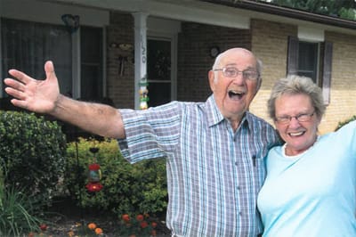 Two smiling seniors posing outside their home
