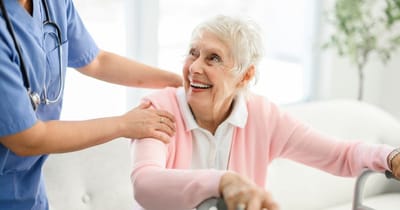 Caregiver assisting a smiling elderly woman indoors