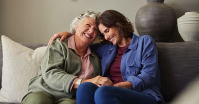 Two women smiling and holding hands on a couch