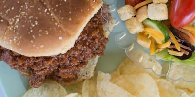 A plate of sloppy joe with salad and chips