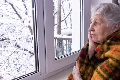 An elderly woman gazing out the window at snowy scenery