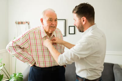 A senior man getting dressed with assistance in a cozy interior
