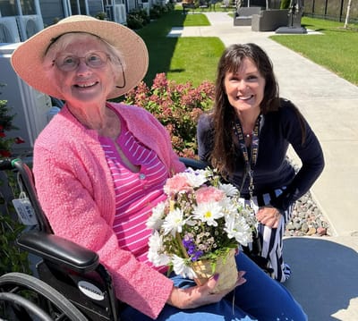 Resident and staff member smiling outdoors with flowers