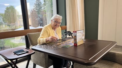 An elderly woman working on a jigsaw puzzle in a bright interior