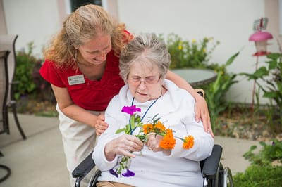 A caregiver assisting a resident with flowers in a garden