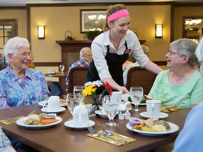 Staff serving residents at a dining table with food
