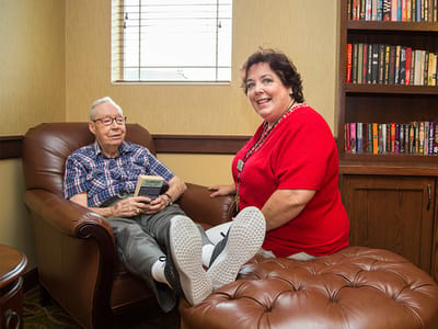 A resident enjoying a book with staff in a cozy living area