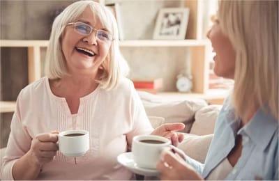 Two elderly women enjoying coffee and laughter in a cozy setting