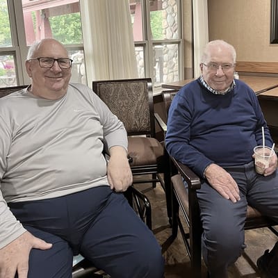 Two elderly men sitting in a common area with drinks
