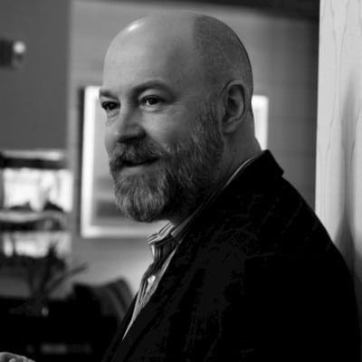 A man with a beard, dressed formally, looking thoughtful.