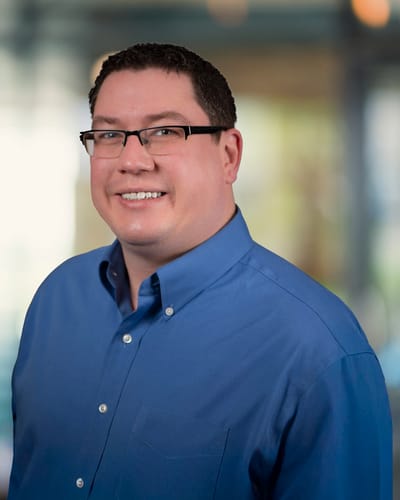A smiling man in a blue shirt with blurred background