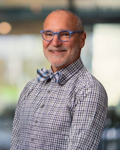 A man smiling in a checkered shirt and bow tie