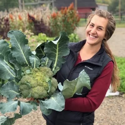 A woman smiling with a large broccoli harvest